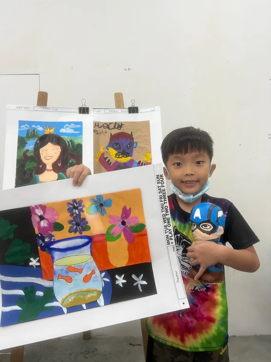 Child displaying paintings and a decorated character sculpture.
